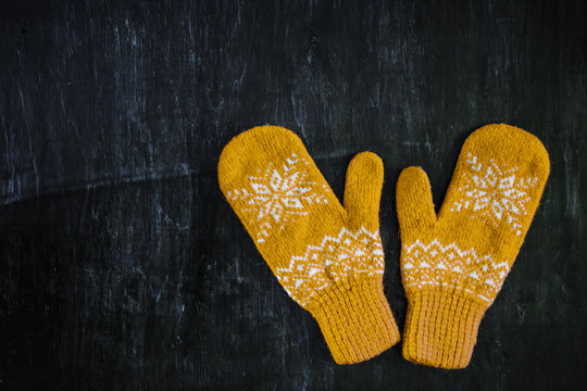 a pair of yellow orange knitted mittens on a dark blue-green-brown wooden