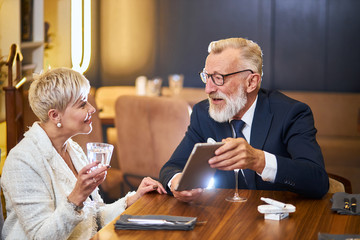 Man in elegant tuxedo and woman use tablet pc. Man holding tablet in hand. speak, chat with each other