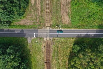 Aerial drone top down view on railroad crossing with asphalt road in the forest with car passing