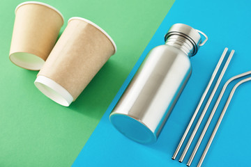 Zero waste eco friendly concept. Reusable plastic free items on a colorful blue and green background. Top view of aluminun bottle, metal tubes and paper coffee cups