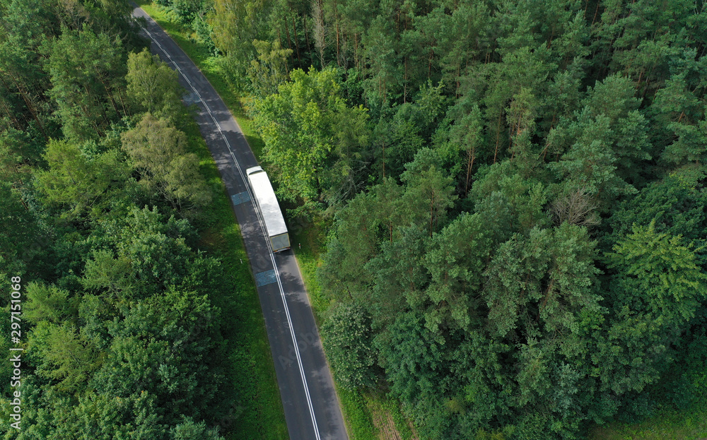 Wall mural Aerial drone perspective view on white truck with cargo trailer riding through the forest on curved asphalt road