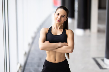 Smiling sports woman standing with arms folded and looking at camera at gym