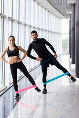 Young Couple standing and keeping resistance band on hips wearing sportswear and trainers at gym