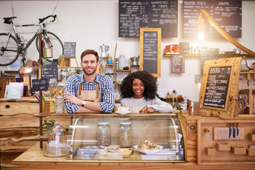 Two smiling diverse baristas standing behind a cafe counter