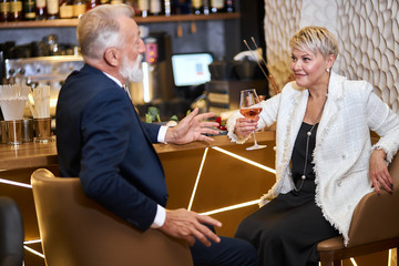 Caucasian man in tuxedo and woman in white blazer have conversation, smile and happy together in love. Background elegant expensive restaurant
