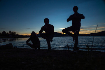 silhouette of three people doing yoga during sunset next to lake