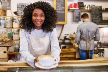 Fototapeta na wymiar Smiling African American barista holding up a fresh cappuccino