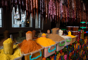 A market counter with containers full of traditional georgian seasoning below glossy churchkhela, local sweets made of nuts in hardened thick grape juice syrup.