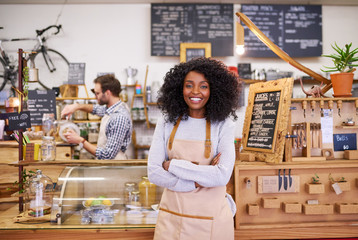 Smiling young African American female barista standing in her cafe - Powered by Adobe