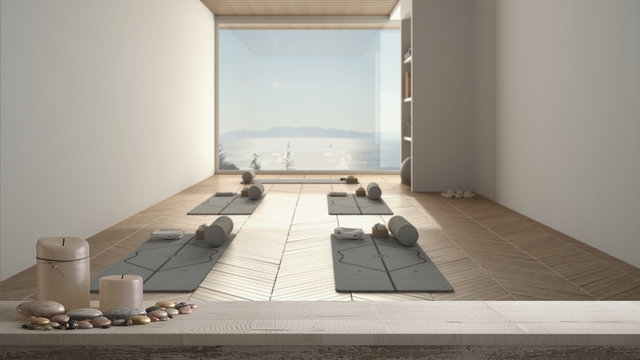 Wooden vintage table top or shelf with candles and pebbles, zen mood, over empty yoga studio, mats and accessories, window with sea panorama, ready for yoga practice, meditation room