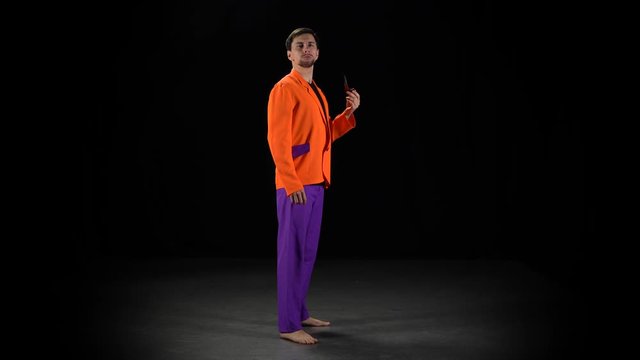 Man in a bright suit and barefoot stands and smokes with a pipe gazing intently at the camera