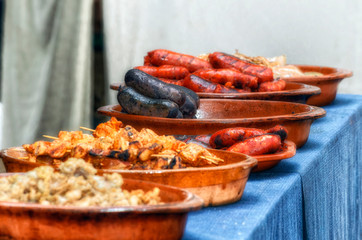 Different meats cooked at outdoor by a street restaurant. Focus in blood sausages. Barbecue with spicy pork sausage, pork rind and morunos skewers. Typical of Spain in festivals and fairs.