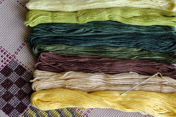 Set of multi-colored cotton threads and fragment of colorful cross-stitch embroidere. Top view....