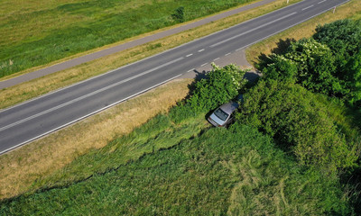 Aerial drone perspective view on car accident hitting the bushes and roadside, high speed on curve causing the car to fell of the road.