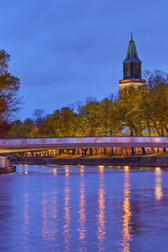 The evening view of Aura river in Turku, Finland with a clock tower of cathedral and bridge on a background.