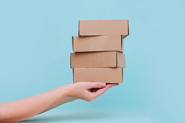 Woman's hands holding boxes stacked on blue pastel background. Mock up.