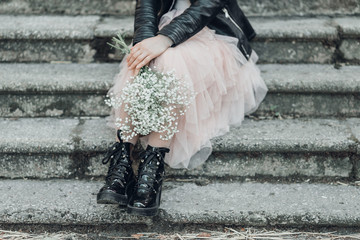 Woman in pink lace skirt with white flowers bouquet in her hands is sitting on stairs.