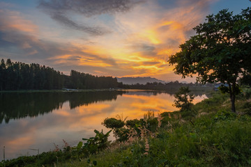 Naklejka na ściany i meble Beautiful view of twilight silhouette sunset on the water reservoir while the sky after sunset has orange light coming out of the clouds and reflecting with the water in the reservoir.