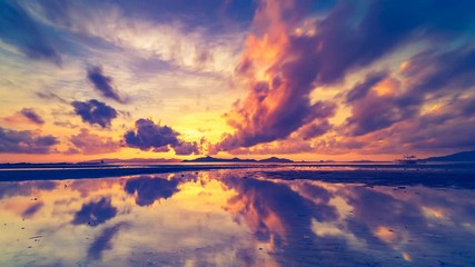 Boundless coloured evening clouds float lit by setting sunlight reflecting in ocean against hill silhouettes time lapse, Thailand - Powered by Adobe