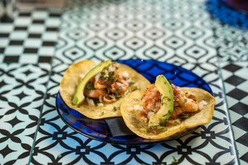 Real Mexican Tacos on a plate. Shrimp tacos with homemade salsa, limes and parsley on wooden board over dark background. Top view. Mexican cuisine
