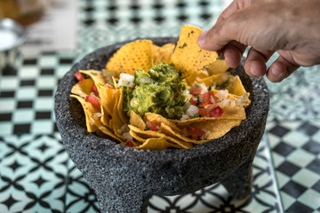 Man taking Yellow corn nacho chips garnished with ground beef, guacamole, melted cheese, peppers...