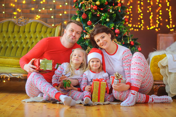 Portrait of a happy family in pajamas, sitting in pajamas near the Christmas tree with puffs in their hands and having fun