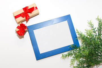 Gifts in craft paper with a red bow on a white background. Blue frame with space for your text. Green twig in the lower floating corner.
