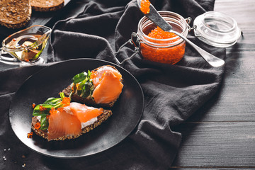 Tasty sandwich with red caviar on dark table