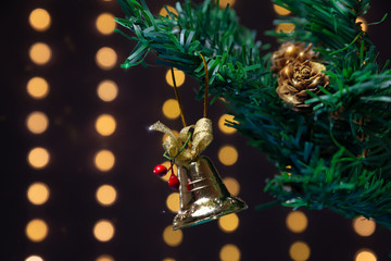 There is gold bell with bow and rowan berry on the green xmas tree branch with shiny cones. There are glowing lights/bokeh and on the background. Merry Christmas. Happy New Year 2020. 