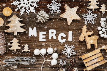 White Letters Building The Word Merci Means Thank You. Wooden Christmas Decoration Like Tree, Sled And Star. Brown Wooden Background With Snowflakes