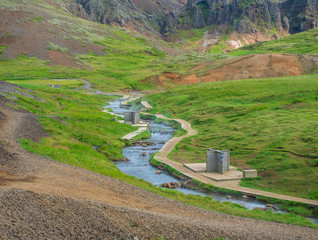 Natural geothermal bath in a Hot River stream in Reykjadalur Valley with wooden footpath and changing rooms. South Iceland near Hveragerdi city. Summer sunny morning