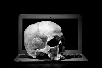 Cybercrime or hacking concept. Laptop in dark room under beam of light with a skull. Idea of virus...