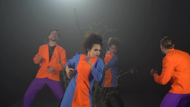 Four psychopath people run around branches, stop and look around on a black studio background with haze.
