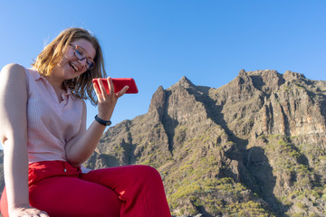Smiley Lady recording a voice message in her smart phone and sending. Woman laughing while hear an...