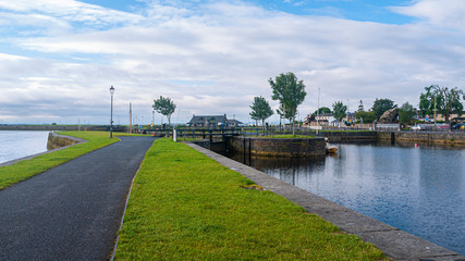 Footpath through park at Galway quay in the city, with trees, grass & sea on a sunny summer day.