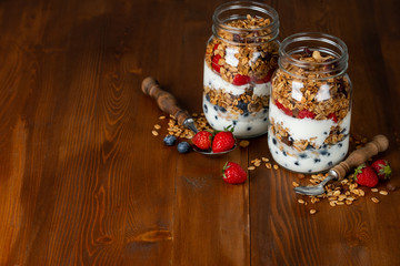 Healthy diet breakfast with granola, yogurt, fruits, berries glass jars on wooden background.