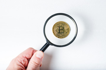 Bitcoin coin through a magnifying glass in a male hand.