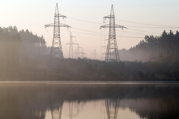 Power line in the cleared area of the forest. Steel electro masts with wires by the lake.