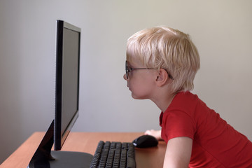 Blond boy with glasses sits his nose buried in a monitor. Internet and preschooler