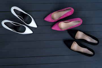 Three pairs of different high heel shoes. Black wooden background.