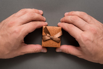 Brown jewelry box in man hands. Present. Black background. Top view