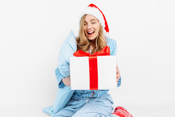 Christmas morning. Happy beautiful young girl, in Christmas pajamas and Santa hat, received a gift on Christmas day