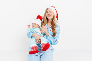 Obraz premium A young mother, on Christmas day gives a gift to a newborn child, a girl holds a baby in her arms in a Christmas hat