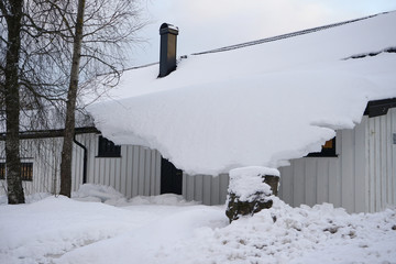 Snow overhangs from the roof of the house.