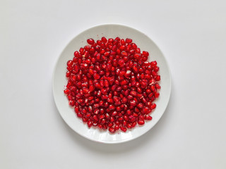 Peeled red pomegranate seeds in a white plate