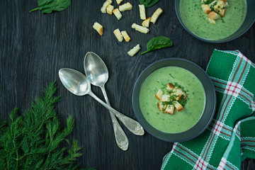 Creamy spinach soup with crackers, herbs and chia seeds. Green soup served in a bowl on a wooden...