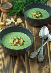 Creamy spinach soup with crackers, herbs and chia seeds. Green soup served in a bowl on a wooden table. Flat lay.