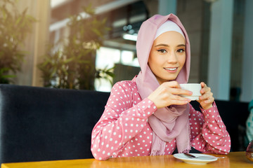 beautiful young woman in muslim dress is drinking tea in a restaurant
