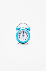 Right timing. A light-blue alarm clock with a black and white clock face, placed on a white background. Clock hands show 12 o’clock.