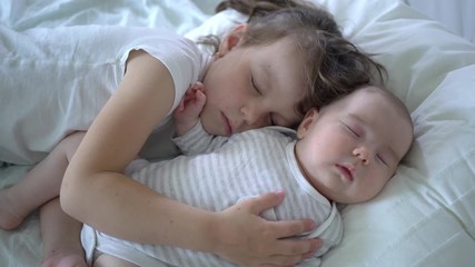 Older sister and the newborn baby sister sleeping together. Two little girls are lying on the bed. Concept of love and child care. 